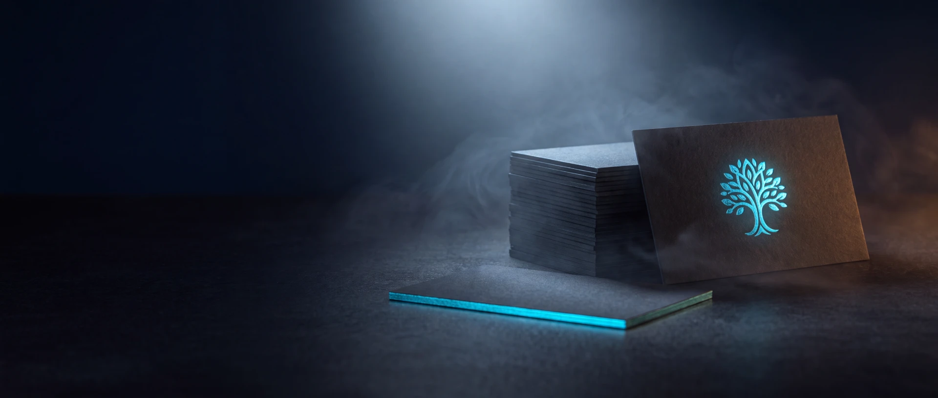 Matte black business cards with a cyan foil mark, fanned out on a cutting mat.